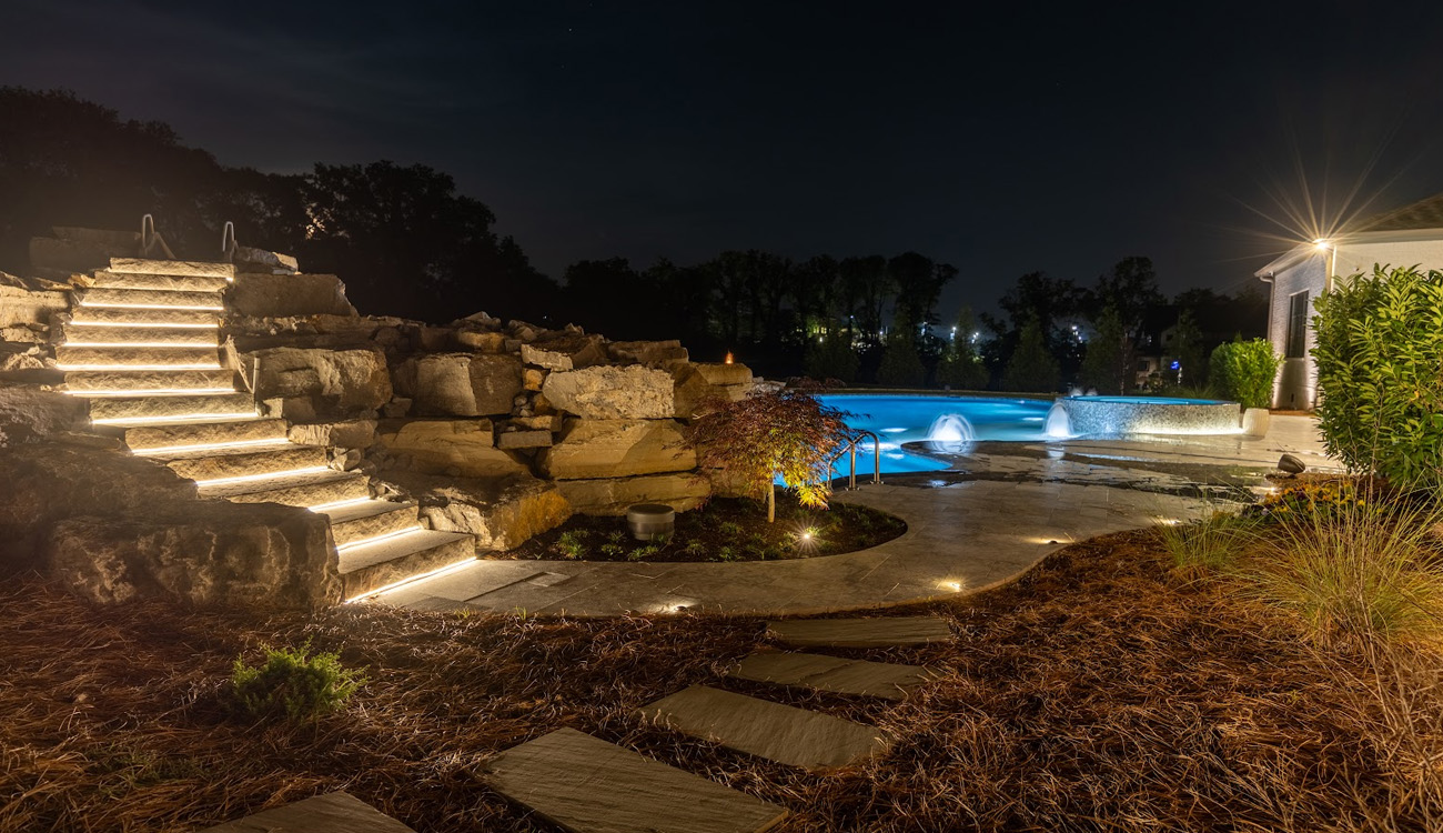 Stone steps illuminated beside a backyard pool