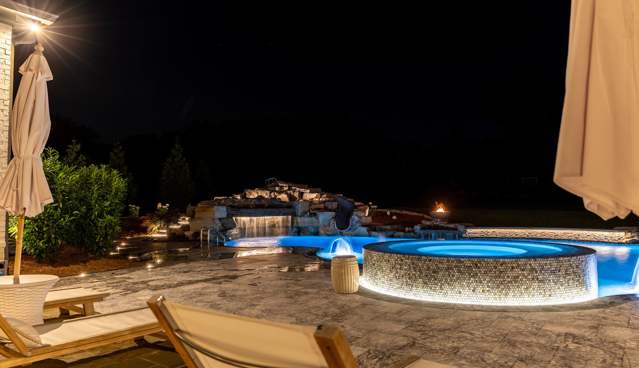 Illuminated circular spa and poolside patio at night