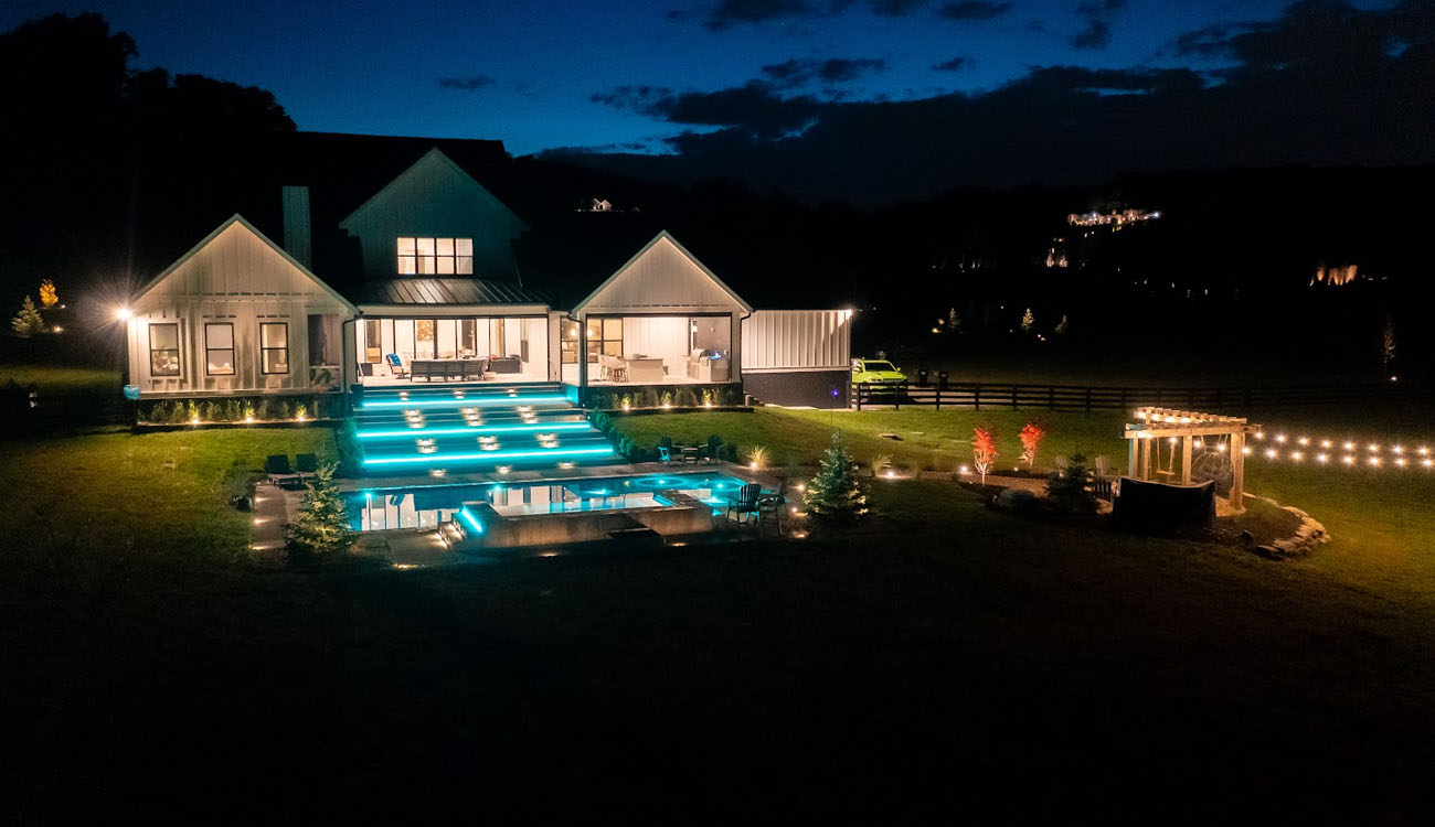 Terraced pool and backyard lighting below a large home