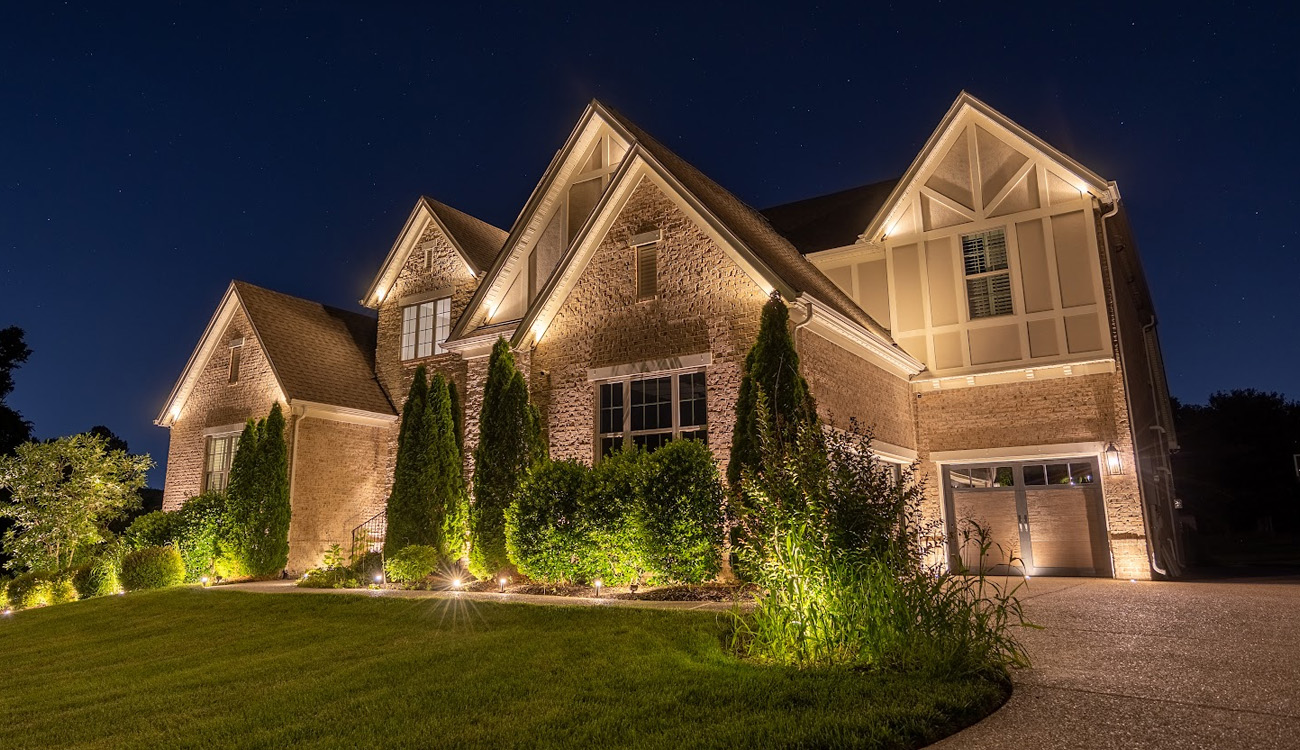 Warm lighting highlighting a home's gables and landscaping