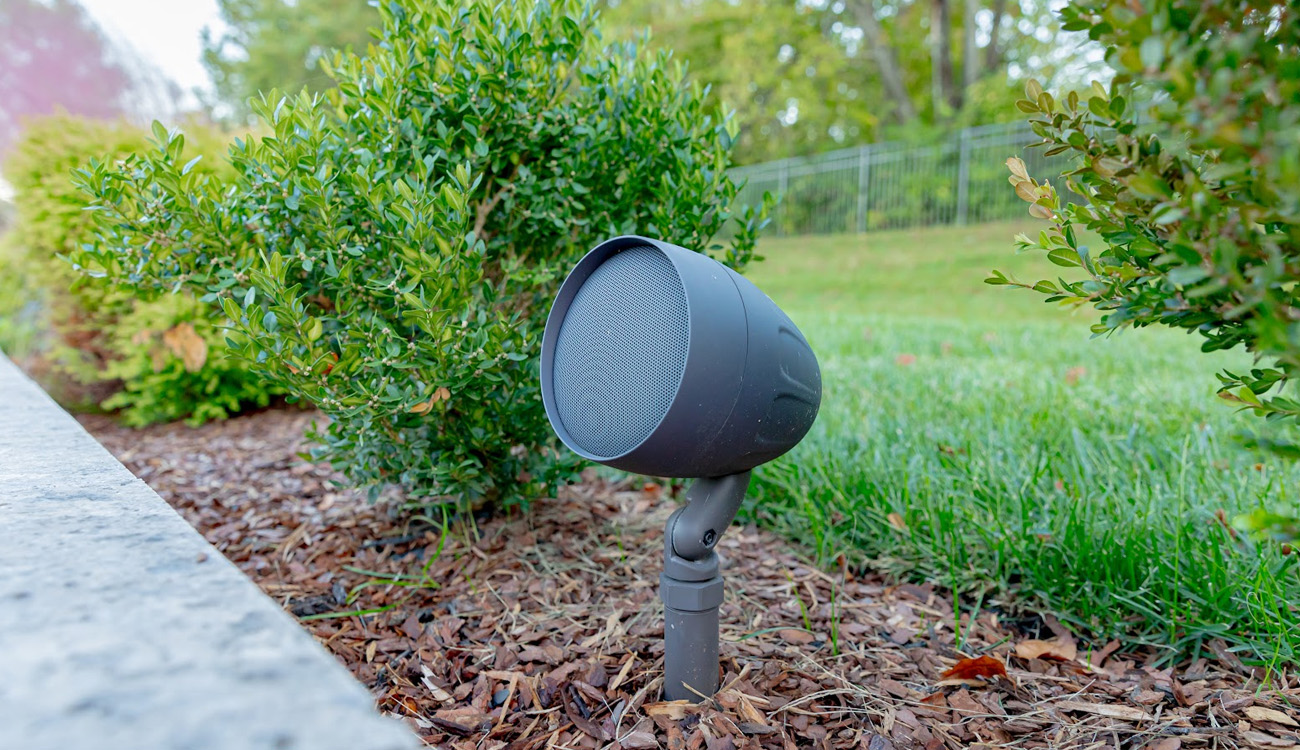 Outdoor speaker installed in a planting bed beside a lawn