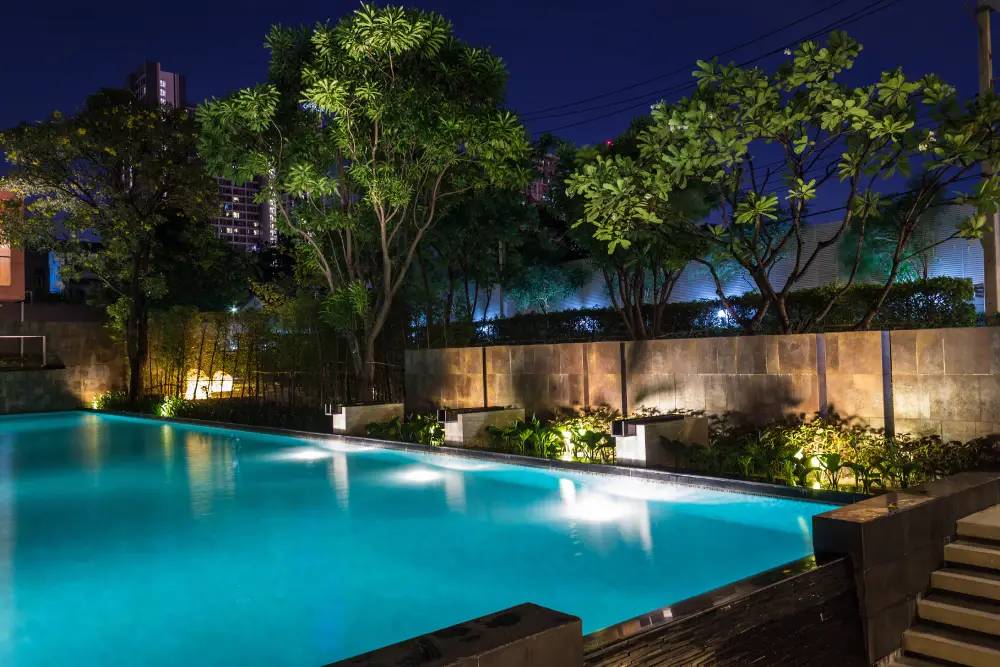 Turquoise pool lighting beside illuminated trees and fencing