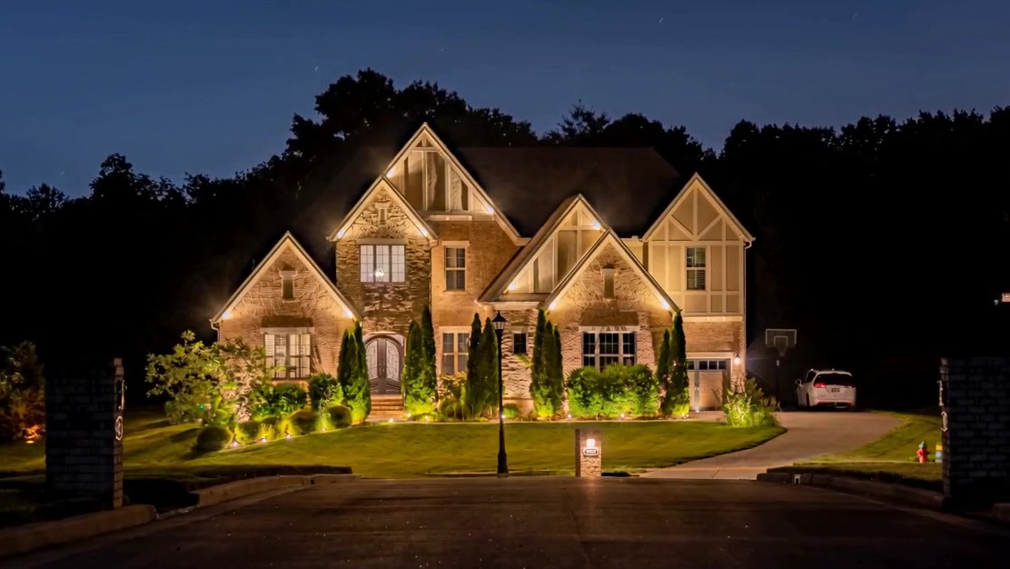 A brick and stone home with warm architectural uplighting and softly illuminated landscaping