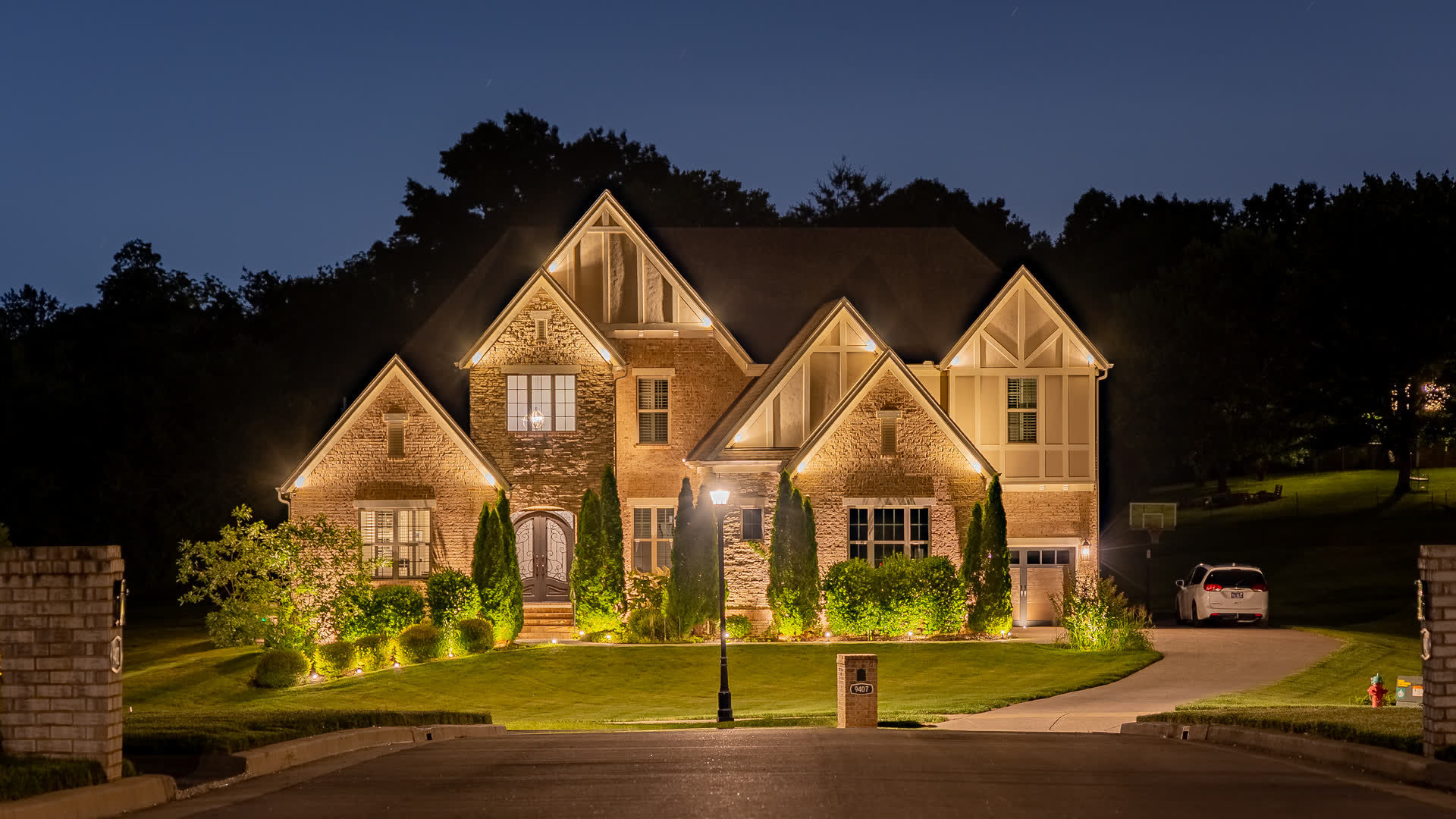 A brick and stone home with warm architectural uplighting and softly illuminated landscaping